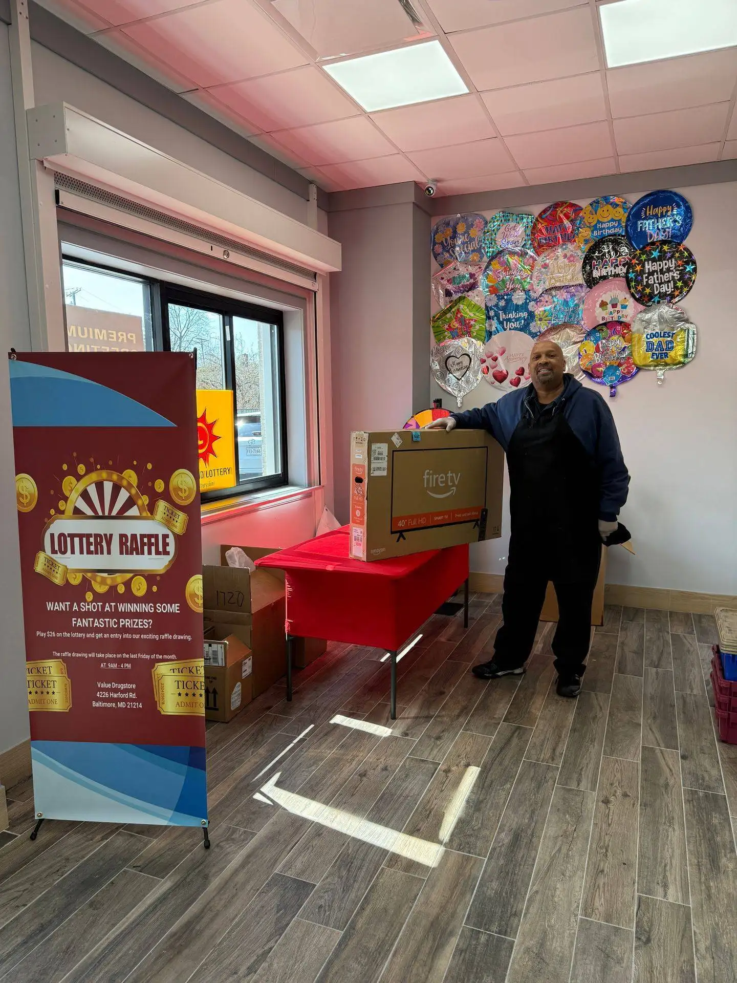 Man holding a Fire TV box next to a lottery raffle banner in Value Drugstore, showcasing promotional prizes and customer engagement.