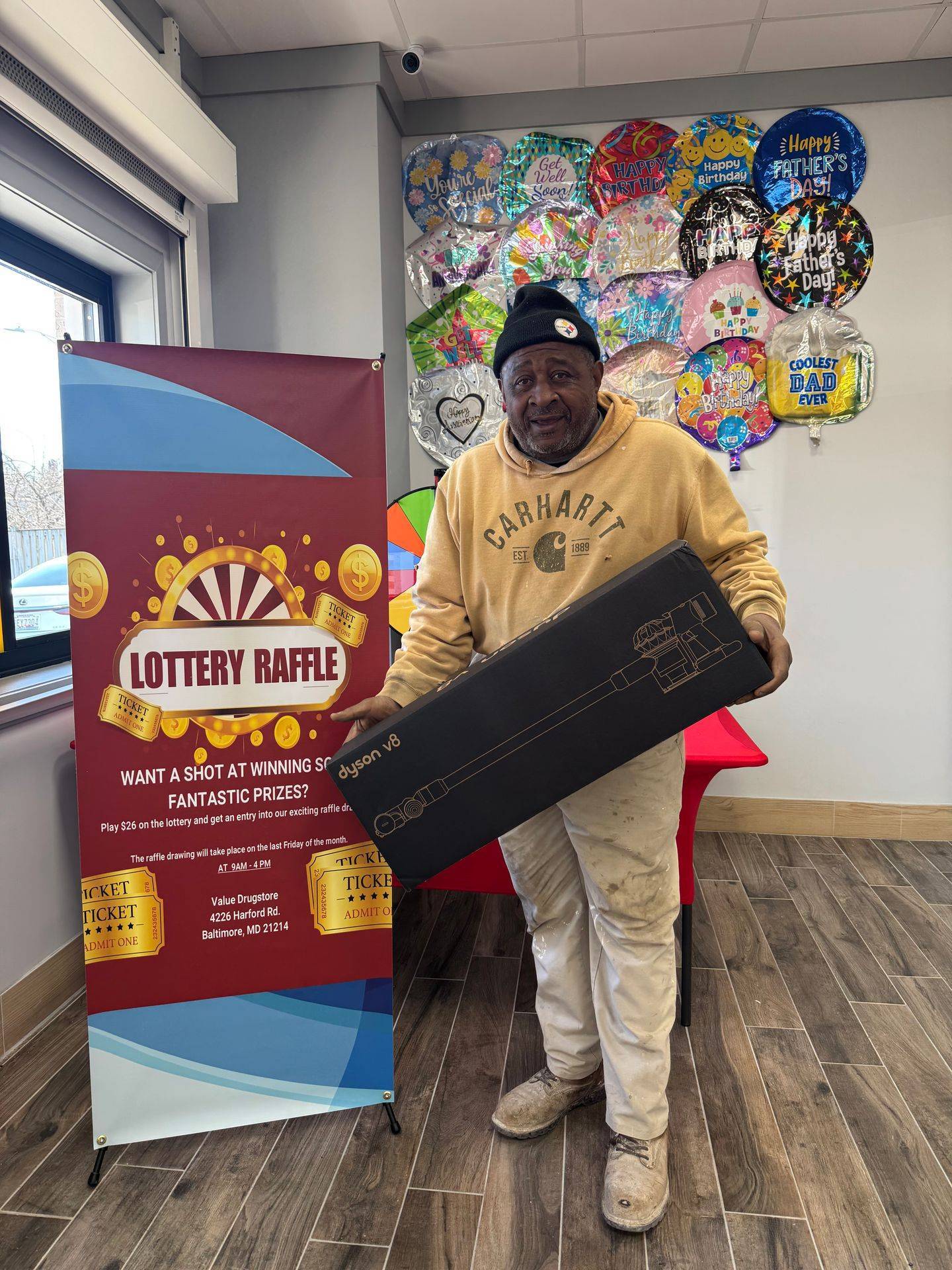 Man holding a Dyson V8 vacuum cleaner box next to a lottery raffle banner at Value Drugstore, promoting fantastic prizes and entry details.